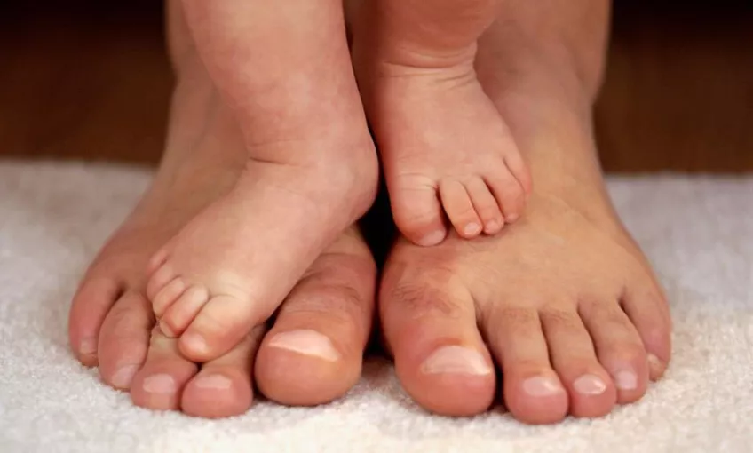 Spädbarns fötter på vuxna fötter. Foto.